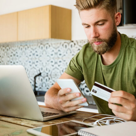 Decorative Image: Male at kitchen table with credit card and phone in hands