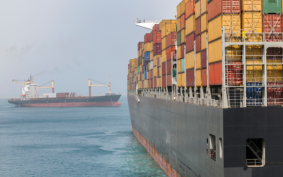 two cargo ships loaded with shipping containers on a calm sea.