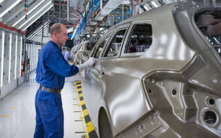 Photo: worker cleaning up car shells on a production line