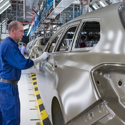 Photo: worker cleaning up car shells on a production line