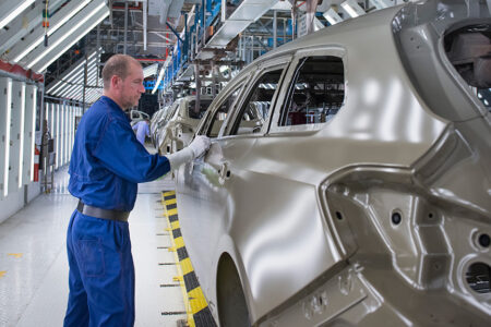 Photo: worker cleaning up car shells on a production line