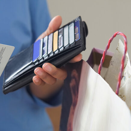 Photo: man holding a wallet in one and a credit card in another with a bag next to him.