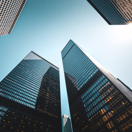 Photo: upward looking at tall glass skyscrapers that are corporate offices against a blue sky.