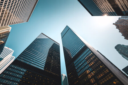 Photo: upward looking at tall glass skyscrapers that are corporate offices against a blue sky.