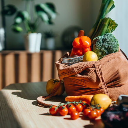 Photo of groceries including peppers, broccoli, lemons and eggs, on a kitchen table in a reusable shopping bag.