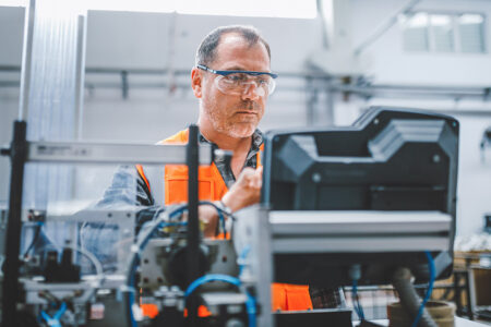 photo: Male industrial worker working with manufacturing equipment in a factory.
