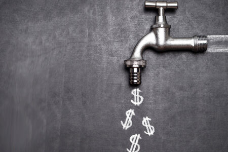 Decorative photo of silver spigot on blackboard with dollar signs chalked on the board coming out of the spigot.