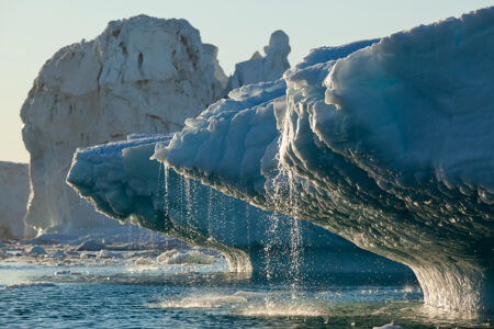 Photo of a melting iceberg with water trickling down splashing into a water body.