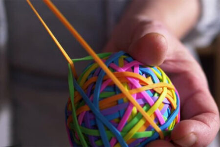 Decorative image: Man pulling an orange rubber band, holding a rubber band ball