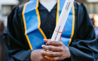 Decorative photo: Young Male Decorative photo: Student In Graduation Gown holding a student loan invoice as the rolled up degree