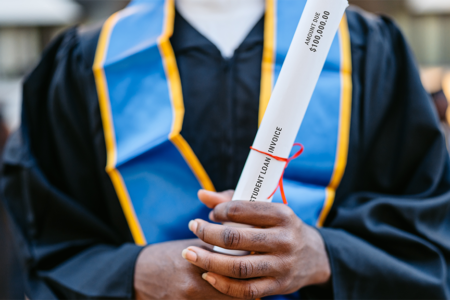 Decorative photo: Young Male Decorative photo: Student In Graduation Gown holding a student loan invoice as the rolled up degree