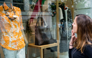 Attractive brunette window shopping looking into boutique. Outdoor store selling luxury items.