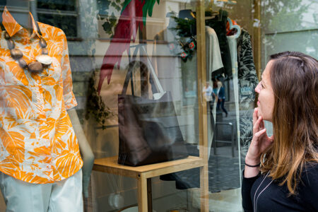 Attractive brunette window shopping looking into boutique. Outdoor store selling luxury items.
