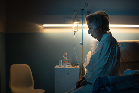 Lonely senior patient suffering from insomnia and sitting on the hospital bed at night