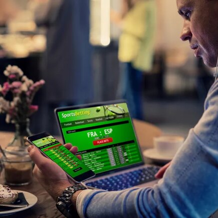 Man using online sports betting services on phone and laptop