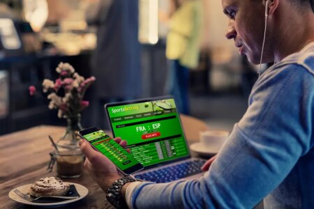 Man using online sports betting services on phone and laptop