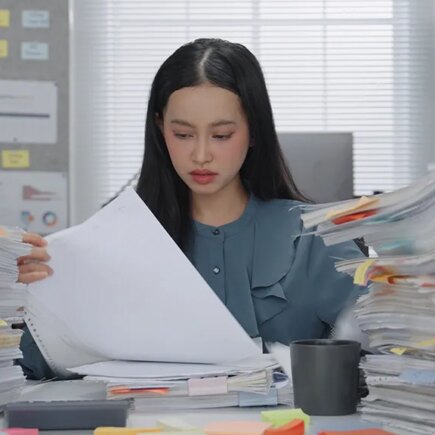 Asian Business woman working busy with massive stacks of documents check and review preparation data report or organizing paperwork workplace stress and administrative overload