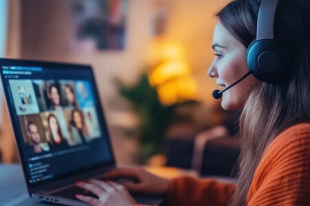 Photo of young caucasian woman working at her desk at home wearing a headsset and engaged in a videoteleconferencing call on her laptop computer.