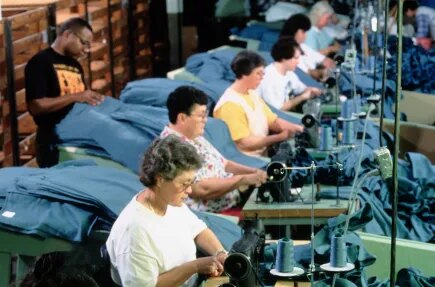 Photo d'hommes et de femmes assis devant des machines à coudre, tous d'affilée, manipulant du tissu bleu.