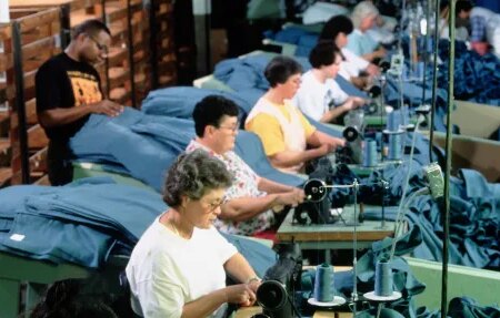 Photo d'hommes et de femmes assis devant des machines à coudre, tous d'affilée, manipulant du tissu bleu.