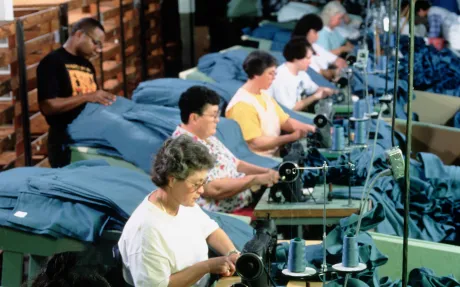 Photo d'hommes et de femmes assis devant des machines à coudre, tous d'affilée, manipulant du tissu bleu.