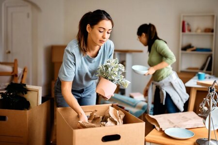 Young woman and her friend packing their belongings while preparing to move out of apartment.