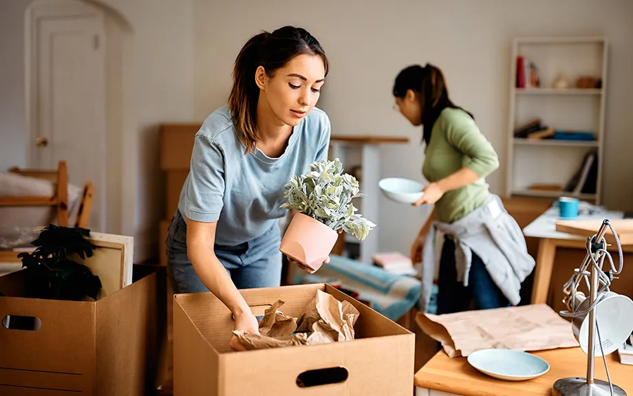 Young woman and her friend packing their belongings while preparing to move out of apartment.