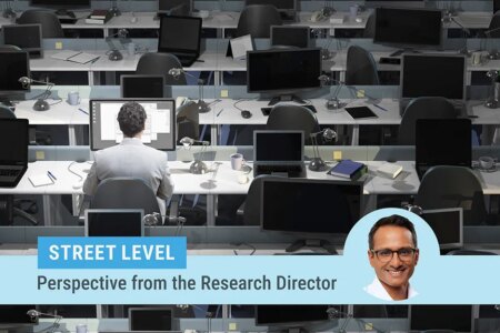 Street level column by Research Director Kartik Athreya. Image of Athreya on top of a photo of a large room with rows of desks and laptops with only one man sitting at one desk working.