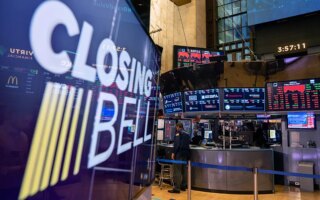 Floor of the stock exchange with a large screen in front that says closing bell.