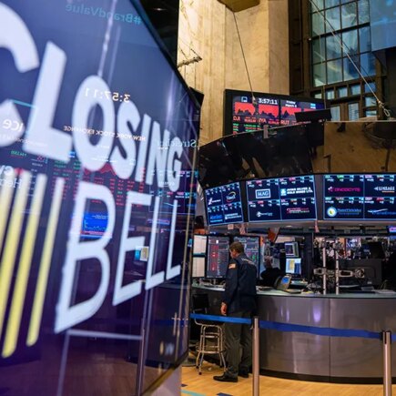 Floor of the stock exchange with a large screen in front that says closing bell.